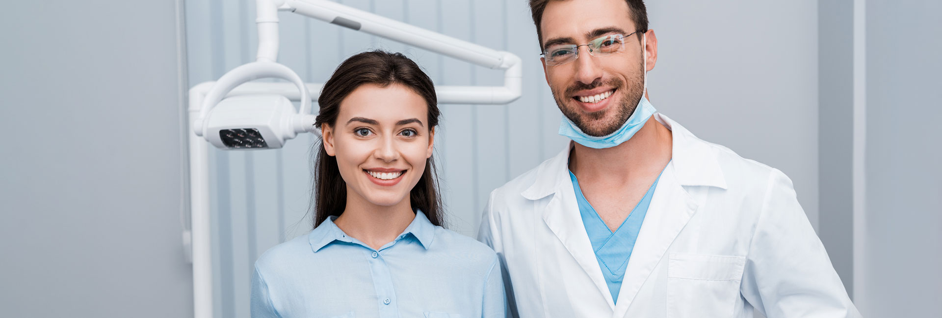 Cheerful girl smiling near handsome dentist standing with hands in pockets